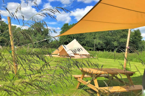 Outdoor view of Bulrush Bell Tent with picnic table on grass field under blue sky in the UK.