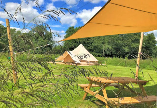 Outdoor view of Bulrush Bell Tent with picnic table on grass field under blue sky in the UK.