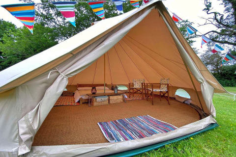 Interior of a teepee tent decorated with colorful bunting, featuring cozy furniture and a woven rug.