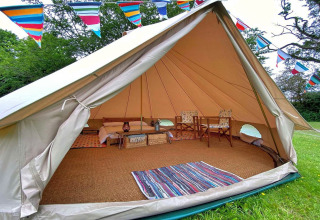 Interior of a teepee tent decorated with colorful bunting, featuring cozy furniture and a woven rug.