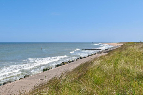 Coastal view with grass, beach, sea, and clear blue sky, as seen from a pathway along the coastline.