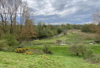 View of lush green landscape, trees, and a river at Bulrush Bell Tent in the United Kingdom under cloudy skies.