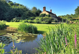 Picturesque glamping site with pond, wildflowers, green lawn and cottage at Meadow Glamping Tents, UK.