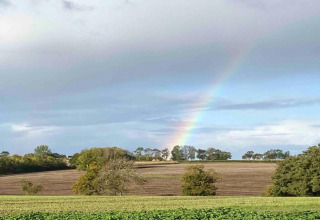 View of fields with a rainbow near Bulrush Bell Tent, a tipi tent in the UK, under a cloudy blue sky.