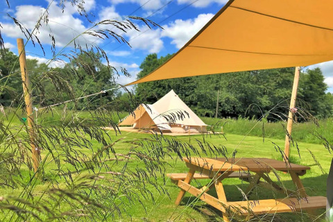 Photo of Meadow Glamping Tents teepee in the UK, showing grassy field, picnic table, and shade canopy.