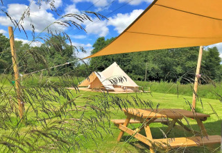 Photo of Meadow Glamping Tents teepee in the UK, showing grassy field, picnic table, and shade canopy.