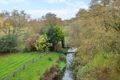 Landscape view from Bulrush Bell Tent, United Kingdom, with green field, trees, and a small stream.