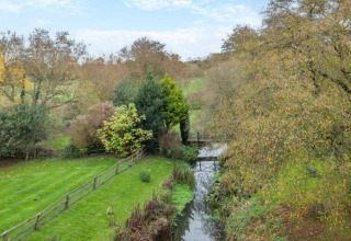 Landscape view from Bulrush Bell Tent, United Kingdom, with green field, trees, and a small stream.