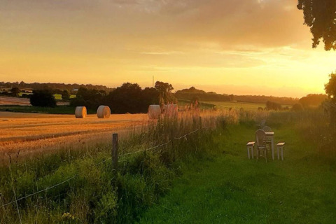 Sunset over fields by Bulrush Bell Tent in the UK, with hay bales and outdoor seating on the grass.