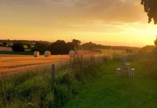 Sunset over fields by Bulrush Bell Tent in the UK, with hay bales and outdoor seating on the grass.