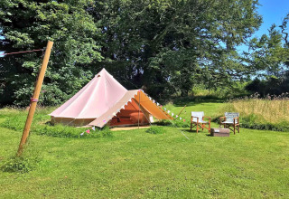 A glamping teepee tent at Meadow Glamping Tents in the UK, set on a green field with trees in the background.