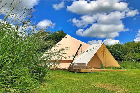 Large teepee tent at 'Meadow Glamping Tents' in the UK, set on green grass under a blue sky.