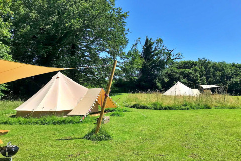 Meadow Glamping Tents in the UK, showing spacious teepee tents and lush green grass under blue skies.