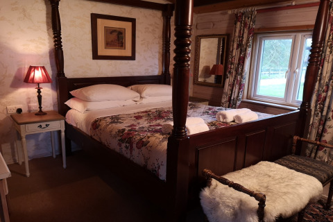 Accogliente camera da letto con letto a baldacchino, biancheria floreale e finestra nella Tore Petty cabin, UK.
