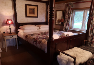 Accogliente camera da letto con letto a baldacchino, biancheria floreale e finestra nella Tore Petty cabin, UK.