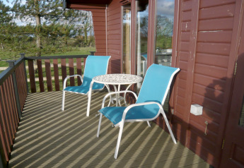 Outdoor deck of Tore Petty cabin in the UK with two blue patio chairs and a round white metal table.