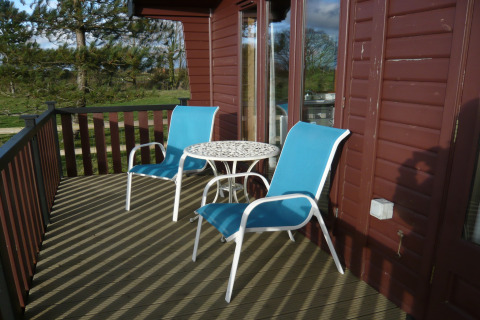 Terrazza esterna della cabina Tore Petty nel Regno Unito con due sedie blu e tavolo rotondo bianco.