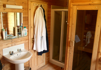 Bathroom with sink, mirror, bathrobes, shower cubicle and sauna inside a wooden cabin in the UK.