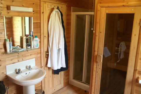 Bagno con lavabo, specchio, accappatoi, box doccia e sauna in una cabina di legno nel Regno Unito.