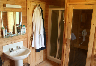 Bagno con lavabo, specchio, accappatoi, box doccia e sauna in una cabina di legno nel Regno Unito.