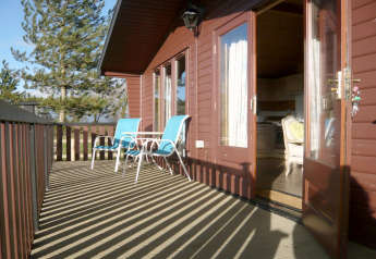 Sunny deck at a wooden cabin named Tore Petty with blue chairs and a table, door open to cozy interior.