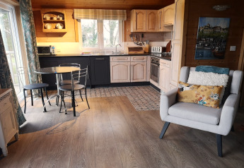 Cozy living area and kitchen in Tore Petty cabin, UK, featuring dining table, armchair, and wood interior.