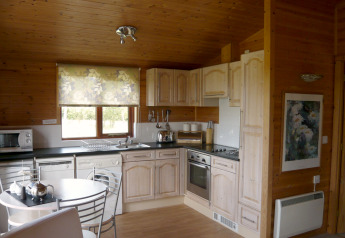 Wood cabin kitchen with light wood cabinets, modern appliances, small dining table and floral window blind.
