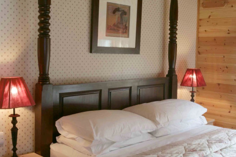 Camera nella baita Tore Petty, Regno Unito, con letto in legno scuro e lampade rosse ai lati.