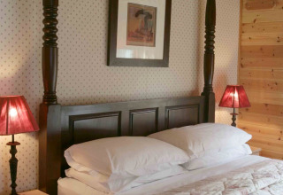 Camera nella baita Tore Petty, Regno Unito, con letto in legno scuro e lampade rosse ai lati.