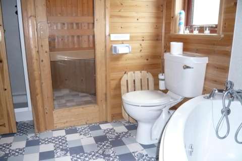 Bagno con pannelli in legno, wc, vasca e sauna in una baita chiamata 'Tore Petty' nel Regno Unito.