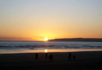 Sunset over the sea viewed from the beach at the Tore Petty cabin, with silhouetted people in the foreground.