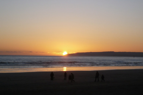 Tramonto sul mare visto dalla spiaggia vicino alla baita Tore Petty, con persone in silhouette in primo piano.