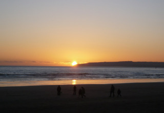 Tramonto sul mare visto dalla spiaggia vicino alla baita Tore Petty, con persone in silhouette in primo piano.