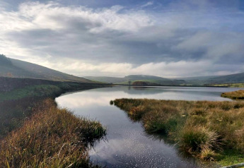 View from Tore Petty cabin in the United Kingdom showing a calm lake, grassy banks and distant hills.