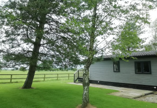 Vista su prato verde, alberi e una baita grigia chiamata 'Tore Petty' nella campagna britannica.