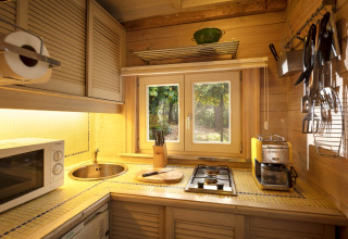 Accogliente cucina in legno con fornello, lavello e finestra sul bosco nello chalet Het Beerenbos, Belgio.