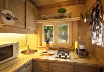 Acogedora cocina de madera con estufa, fregadero y ventana al bosque en chalet Het Beerenbos, Bélgica.