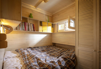 Acogedor dormitorio de madera con estantes de libros y ventana abierta en el chalet 'Het Beerenbos' en Bélgica.