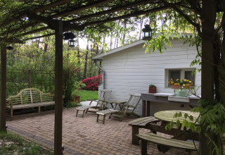 Patio esterno dello chalet Het Beerenbos in Belgio con panchine in legno e sedie sdraio tra il verde.