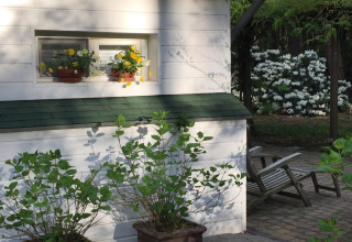 Chalet bianco a Het Beerenbos in Belgio con fiori in vaso sulla finestra e giardino verde sullo sfondo.