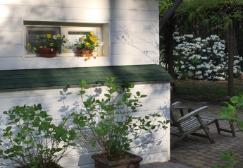 Chalet blanco en Het Beerenbos, Bélgica, con macetas de flores en la ventana y jardín verde detrás.