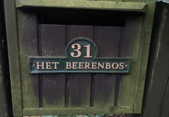 El número 31 y el letrero 'Het Beerenbos' en la puerta de madera de un chalet en Bélgica con musgo.