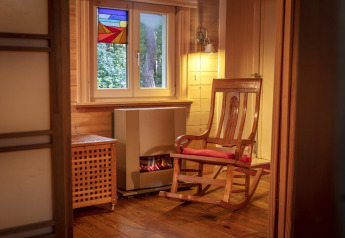 Rincón acogedor con mecedora, chimenea y vitral en el chalet Het Beerenbos de Bélgica.
