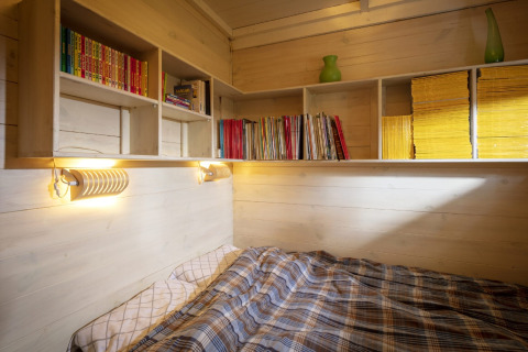Accogliente angolo notte con mensole di libri, trapunta scozzese e pannelli in legno a Het Beerenbos, Belgio.