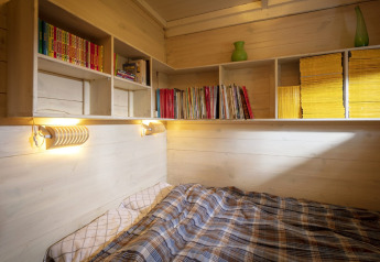 Acogedor rincón para dormir con estanterías, edredón de cuadros y madera en chalet Het Beerenbos, Bélgica.
