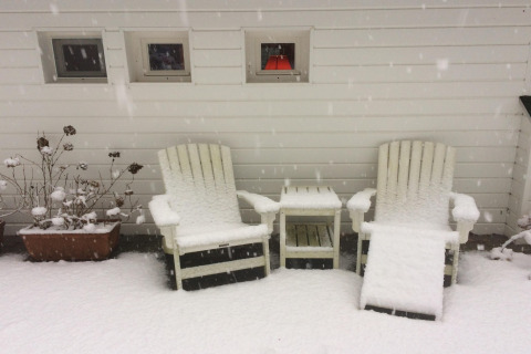 Due sedie da giardino coperte di neve e un tavolino davanti a una parete bianca al chalet 'Het Beerenbos' in Belgio.