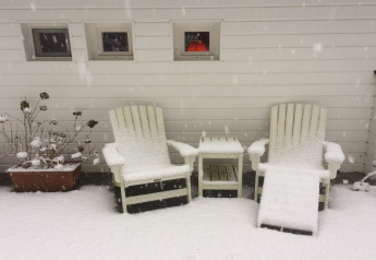 Dos sillas de jardín cubiertas de nieve y una mesa junto a una pared blanca en el chalet 'Het Beerenbos' en Bélgica.