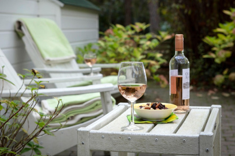 Scena rilassante allo chalet Het Beerenbos in Belgio con vino rosé, snack e sedie a sdraio all'aperto.