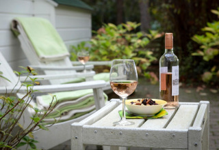 Scena rilassante allo chalet Het Beerenbos in Belgio con vino rosé, snack e sedie a sdraio all'aperto.