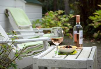 Escena relajante en el chalet Het Beerenbos en Bélgica con vino rosado, bol de aperitivos y sillas al aire libre.